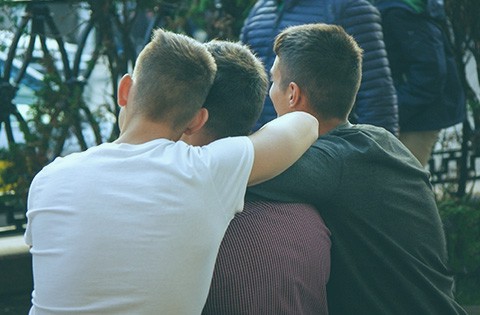 photo showing the back of three friends with their arms around their shoulders