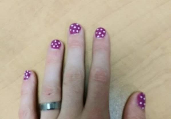 A hand of a guy wearing pink nail polish with white polka dots.